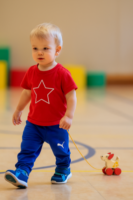 Toddler pulling a wooden Montessori dog toy across a classroom floor.