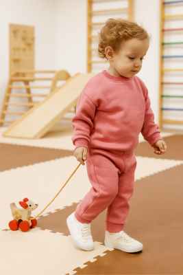 Toddler pulling a wooden Montessori dog toy across a classroom floor.